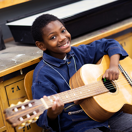 student smiling while playing guitar